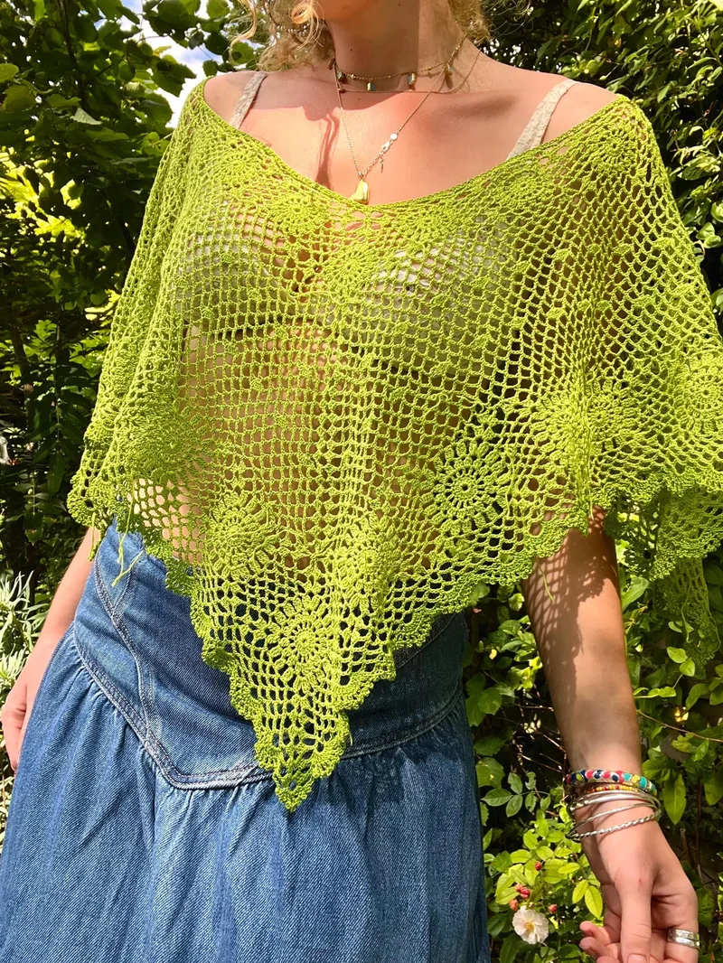 Lime green openwork Clover Poncho with floral motifs and a pointed scalloped hem worn over a denim skirt
