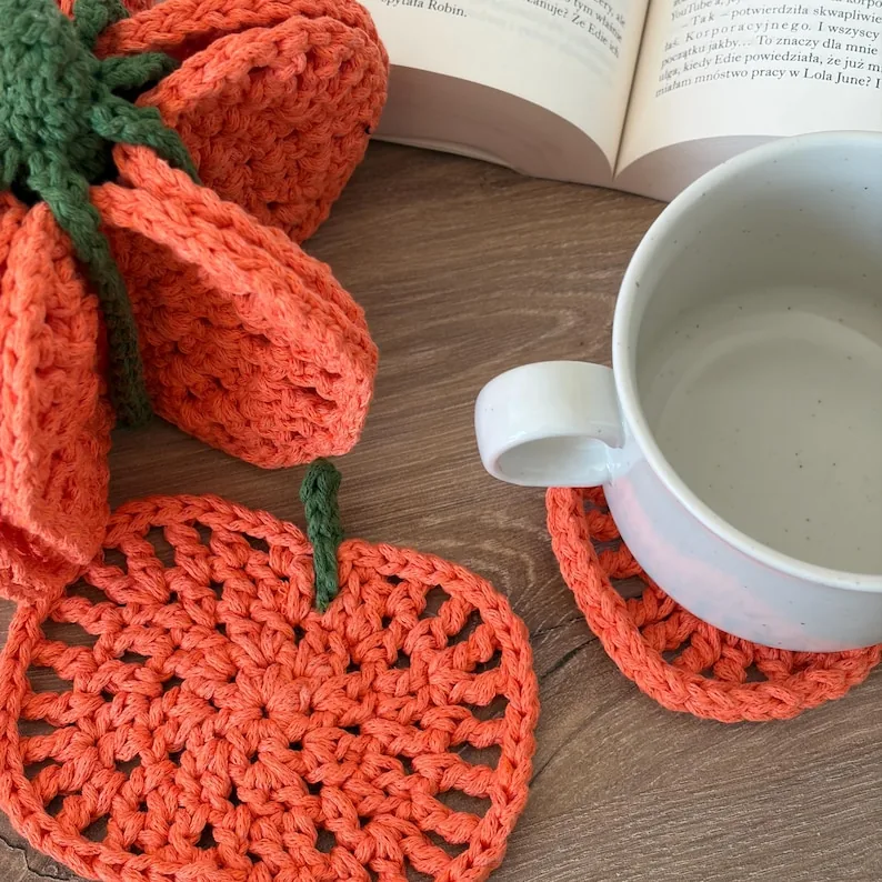 A white cup on an orange crochet coaster with a second pumpkin coaster beside it