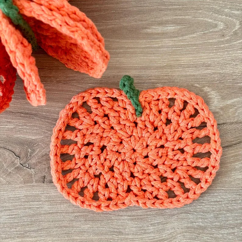 Close view of a flat orange pumpkin crochet coaster showing its open stitches and green stem