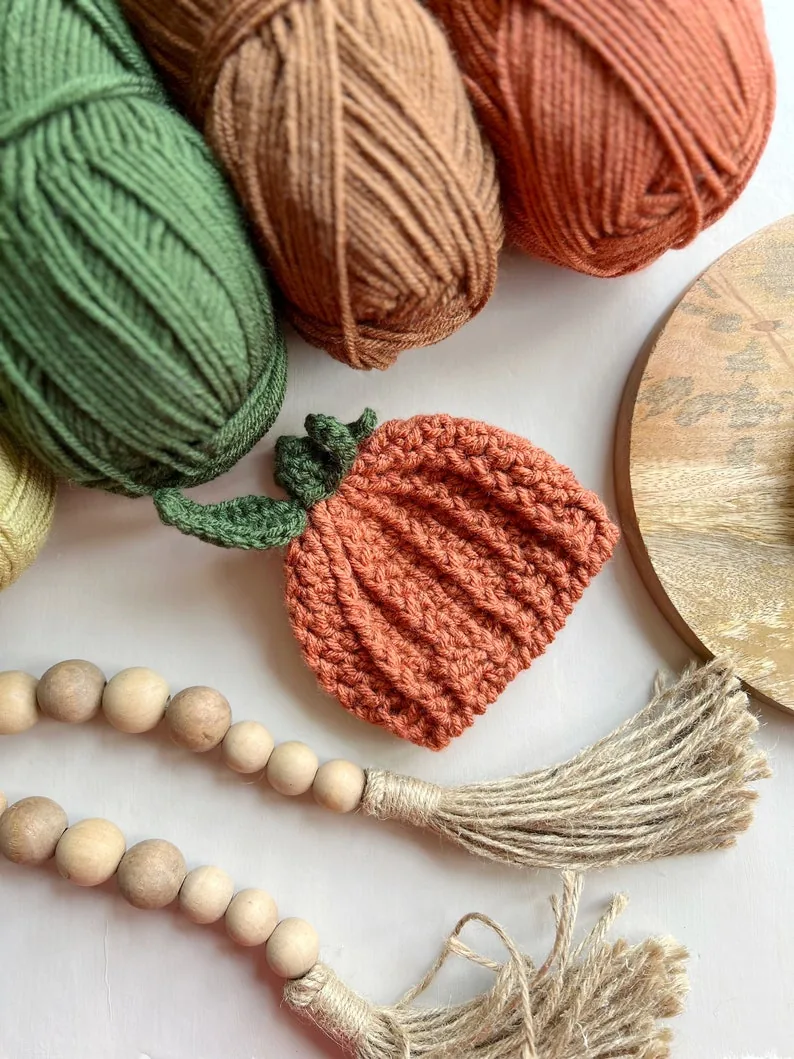 Autumn-toned yarn and a small finished pumpkin beanie arranged for a crochet project